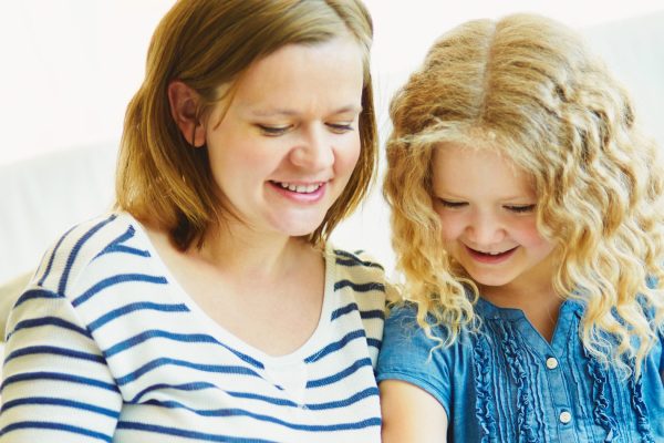 Portrait of cute girl and her mother reading a book at home